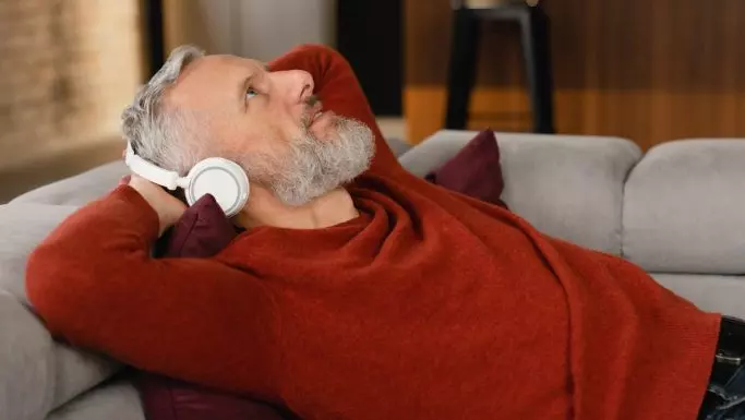 Senior mand ligger i sofa og lytter med høretelefoner
