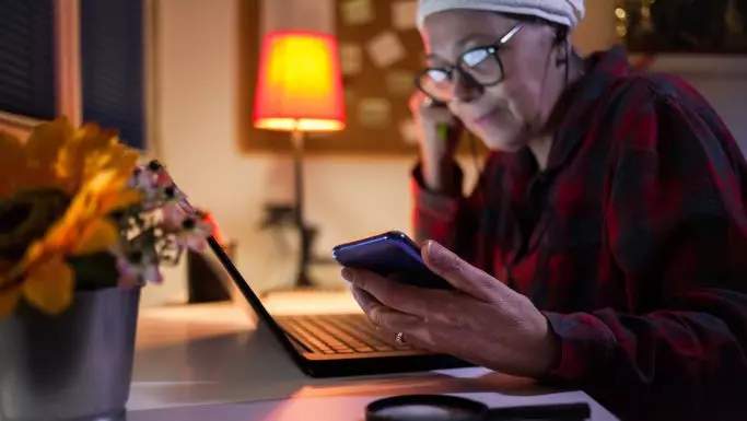 Senior kvinde bruger telefonen som lup ved skrivebordet