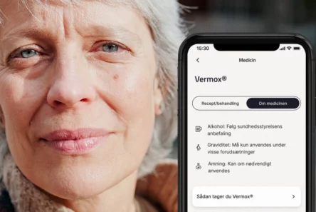 Nærbillede af en ældre kvinde med kort gråt hår ved siden af en smartphone-skærm, der viser information om lægemidlet Vermox, herunder brugsanvisning og sikkerhedsadvarsler på dansk i MinSundhed-appen.