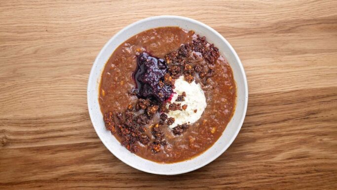 En skål med tyk chili, der minder om moderne komfort, toppet med en klat creme fraiche, smuldret hakket kød og et dryp mørk sauce, serveret på et træbord - en hyggelig guide til smagsoplevelser inspireret af klassisk øllebrød.