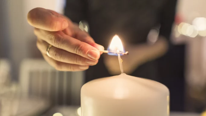 Et nærbillede af en hånd, der tænder et stort hvidt stearinlys med en tændstik. Den let slørede baggrund fremhæver flammen og lyset, mens en ring pryder fingeren - og indfanger et opmærksomt øjeblik, hvor man foretager det sundeste valg.