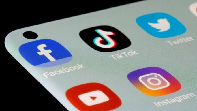 Nærbillede af en smartphone-skærm med ikoner for populære sociale medier: Facebook, TikTok, Twitter, Instagram og YouTube. Ikonerne er farvestrålende på en lys baggrund - og minder brugerne om at være opmærksomme på sundhed og svindlere online.