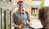 Et smilende bud står ved en hoveddør med en pakke og en tablet i hånden, iført en grå poloshirt og en snor med et ID-badge, mens en ældre person - der er opmærksom på svindel - hilser på dem inde fra huset.