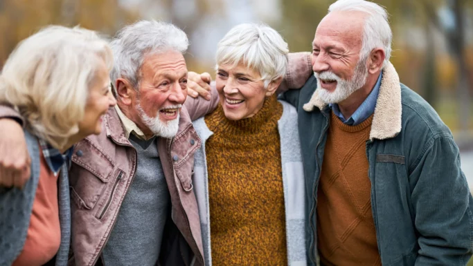 Fire smilende ældre voksne står udendørs med armene om hinandens skuldre, klædt i varmt tøj. De virker glade og engagerede og nyder hinandens selskab - som en venneliste med nogle af de mest udbredte navne.