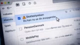 En computerskærm viser en indbakke på dansk. Den valgte mail er fra Skattestyrelsen med et advarselsikon og lyder: Du kan nu se din årsopgørelse. Andre mails er fra PensionDanmark og MobilePay.