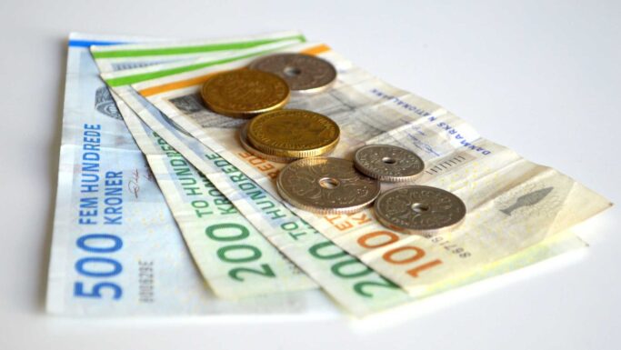Flere danske kronesedler (500 og 200) og mønter er arrangeret på en hvid flade og symboliserer opsparing eller de midler, man kan få, når man går på folkepension.