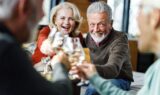 Fire danskere, alle over 30 år, sidder sammen indendørs og nyder hinandens selskab i en hyggelig stue, smilende og grinende, mens de skåler med vin i et varmt og lyst rum - måske fejrer de deres pensionsformue.
