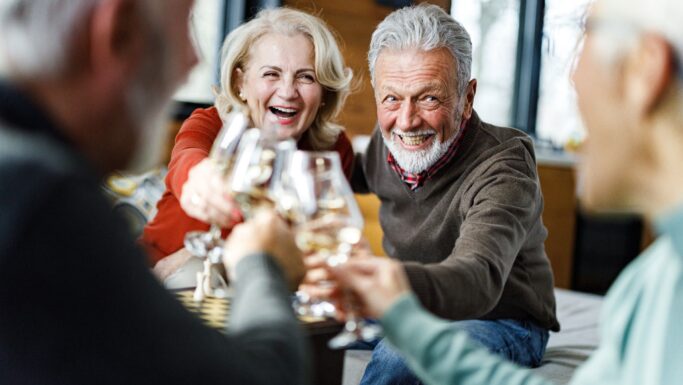 Fire danskere, alle over 30 år, sidder sammen indendørs og nyder hinandens selskab i en hyggelig stue, smilende og grinende, mens de skåler med vin i et varmt og lyst rum - måske fejrer de deres pensionsformue.