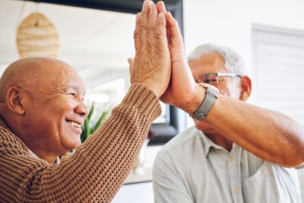 To ældre mænd smiler og giver hinanden en high five indendørs, mens de fejrer en god nyhed om aktiesparekonto loftet og deler et glædeligt øjeblik sammen.