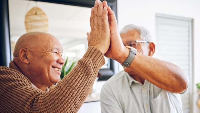 To ældre mænd smiler og giver hinanden en high five indendørs, mens de fejrer en god nyhed om aktiesparekonto loftet og deler et glædeligt øjeblik sammen.