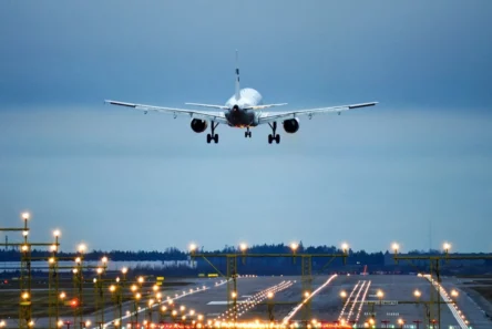 Et passagerfly fra flyselskabet nærmer sig en veloplyst landingsbane for at lande i skumringen, med rækker af landingsbanelys, der viser vejen, og en overskyet himmel over sig.