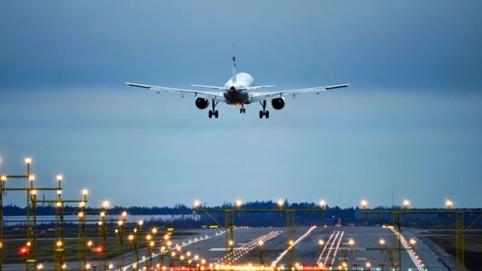 Et passagerfly fra flyselskabet nærmer sig en veloplyst landingsbane for at lande i skumringen, med rækker af landingsbanelys, der viser vejen, og en overskyet himmel over sig.