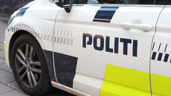 Et nærbillede af en hvid Politiet-politibil med ordet POLITI på siden, gule refleksmærker og et snavset forhjul – en bil, man ofte ser, når betjente rykker hurtigt ud til anmeldelser om svindlere, der har ældre borgere som mål.
