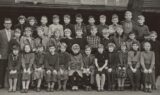 Sort-hvidt foto af en gruppe skolebørn og en mandlig lærer, der står i rækker og poserer til et klassebillede. I forreste række står et tavleskilt med påskriften 5Y. Børnene er klædt i tøj i 1950′er- eller 1960′er-stil, hvilket vækker nostalgiske minder om gamle skolekammerater, som man ser på klassiske skolebilleder.