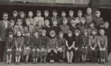 Sort-hvidt foto af en gruppe skolebørn og en mandlig lærer, der står i rækker og poserer til et klassebillede. I forreste række står et tavleskilt med påskriften 5Y. Børnene er klædt i tøj i 1950′er- eller 1960′er-stil, hvilket vækker nostalgiske minder om gamle skolekammerater, som man ser på klassiske skolebilleder.