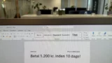 En computerskærm viser et Word-dokument med dansk tekst: »Betal 1.200 kr. inden for 10 dage!« – en besked, der kunne være forbundet med inkassotrusler midt i den aktuelle svindelbølge. I den slørede baggrund ses et kontor med skriveborde, planter og stole.
