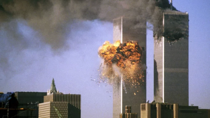World Trade Center-tårnene, hvor det ene tårn er ramt af en eksplosion, med ild og røg, der vælter op; himlen er klar, 25 år efter 11. september.