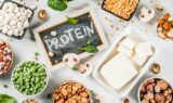 Forskellige plantebaserede proteinkilder, såsom bønner, tofu, ærter, nødder og frø, omgiver en tavle, hvor der står »PROTEIN«. Spredte svampe og spinat fuldender kompositionen – en opstilling, som selv en aldringsforsker ville sætte pris på for dens næringsrige fordele, der er anrettet i indbydende bakker.