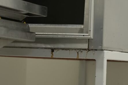 Et nærbillede af en metalkonstruktion med rustpletter og korrosion ved samlingen, der viser tegn på vandskader og forfald, hvilket minder om den slitage, man ofte ser i gammel hospitalsinfrastruktur.