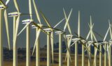 Rækker af hvide vindmøller med Vestas-logoer står på en mark med bakker i baggrunden under en klar himmel og producerer vedvarende energi – et symbol på, hvordan danske aktier som Vestas bidrager til bæredygtige investeringer for fremtiden, herunder investeringer knyttet til pensionskasser.