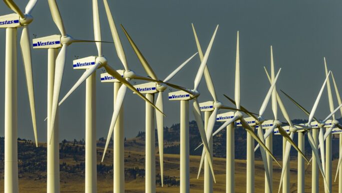 Rækker af hvide vindmøller med Vestas-logoer står på en mark med bakker i baggrunden under en klar himmel og producerer vedvarende energi – et symbol på, hvordan danske aktier som Vestas bidrager til bæredygtige investeringer for fremtiden, herunder investeringer knyttet til pensionskasser.