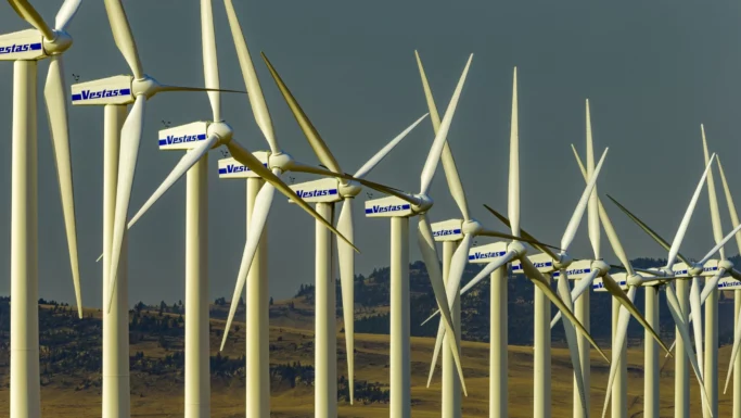 Rækker af hvide vindmøller med Vestas-logoer står på en mark med bakker i baggrunden under en klar himmel og producerer vedvarende energi – et symbol på, hvordan danske aktier som Vestas bidrager til bæredygtige investeringer for fremtiden, herunder investeringer knyttet til pensionskasser.