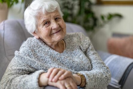 En smilende ældre kvinde med hvidt hår, der sidder i en stol, som repræsenterer de pensionister, der er berettiget til ældrechecken 2027.