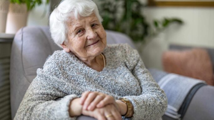 En smilende ældre kvinde med hvidt hår, der sidder i en stol, som repræsenterer de pensionister, der er berettiget til ældrechecken 2027.