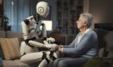 En humanoid robot sidder på en sofa og holder en ældre kvinde i hånden, hvilket illustrerer kunstig intelligens’ rolle i ældreplejen.