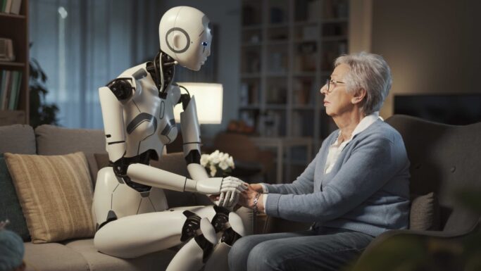 En humanoid robot sidder på en sofa og holder en ældre kvinde i hånden, hvilket illustrerer kunstig intelligens’ rolle i ældreplejen.