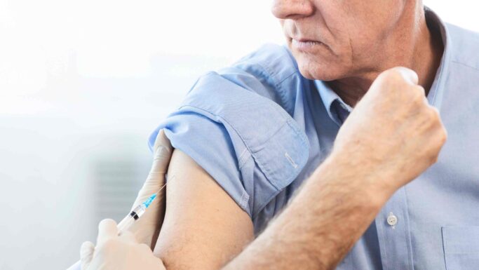 En sundhedsmedarbejder iført handsker, der giver en ældre mand en vaccination i overarmen.