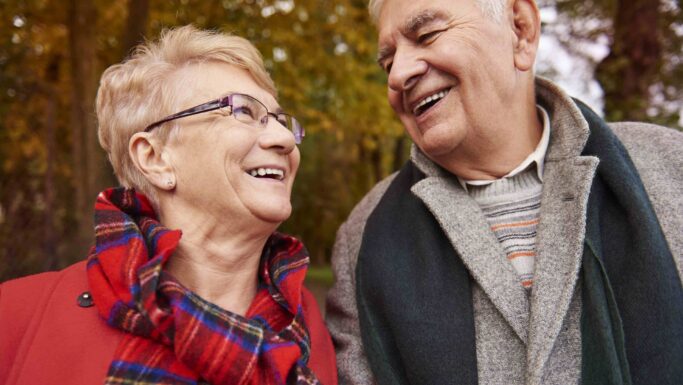Et ældre ægtepar, der afspejler fokus på seniorer i finanslovsforslaget, smiler og ser på hinanden udendørs en efterårsdag.