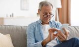 En ældre mand med briller, der kigger nøje på en MobilePay-skærm på sin smartphone, mens han sidder i en sofa.