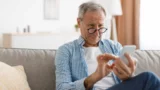 En ældre mand med briller, der kigger nøje på en MobilePay-skærm på sin smartphone, mens han sidder i en sofa.
