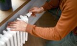 En person justerer temperaturen på en hvid radiator for at gøre sig klar til vinteren og spare på varmeregningen.