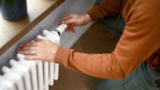 En person justerer temperaturen på en hvid radiator for at gøre sig klar til vinteren og spare på varmeregningen.