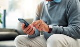 En person, der bærer et ur og en ring, bruger en smartphone til at foretage en MobilePay-betaling.