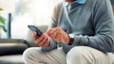 En person, der bærer et ur og en ring, bruger en smartphone til at foretage en MobilePay-betaling.