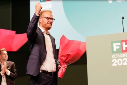 FH-formand Morten Skov Christiansen løfter triumferende knytnæven, mens han holder en buket røde blomster i hånden ved et talerstol med påskriften FH KONGRES 2026.