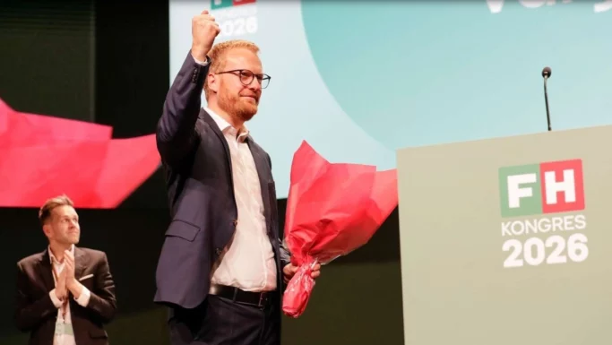 FH-formand Morten Skov Christiansen løfter triumferende knytnæven, mens han holder en buket røde blomster i hånden ved et talerstol med påskriften FH KONGRES 2026.