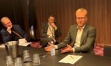 Tre ældre mænd i forretningstøj, der sidder ved et konferencebord under et jobmøde.