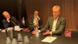 Tre ældre mænd i forretningstøj, der sidder ved et konferencebord under et jobmøde.