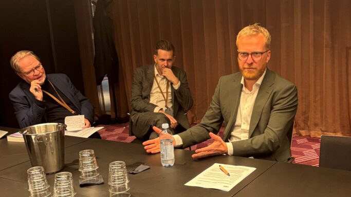 Tre ældre mænd i forretningstøj, der sidder ved et konferencebord under et jobmøde.