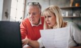 Et ældre ægtepar kigger på et dokument, mens de sammen arbejder på en bærbar computer for at gennemgå regeringens spareplan.