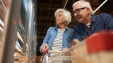 Et ældre par med en indkøbsvogn kigger ind i en køledisk i en dagligvarebutik, opmærksomme på de stigende fødevarepriser.
